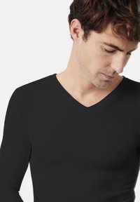 Top negro de manga larga y escote en V, fabricado con una tela suave, que presenta un diseño ajustado que se adapta al cuerpo sin costuras visibles.