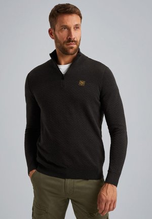 Zwart gebreid pullover met een kwart-rits kraag en een textuurpatroon, met een klein goudkleurig logo op de borst. Lange mouwen en geribde manchetten.
