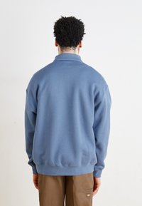 Sweatshirt bleu avec un col montant et des poignets côtelés. Fabriqué en tissu doux, il présente une coupe décontractée et des détails cousus.