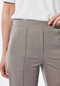 Hellgraue Hosen mit glatter Textur, ausgestattet mit einem breiten Bund, vorderen Falten und Seitentaschen. Einfaches und tailliertes Design.