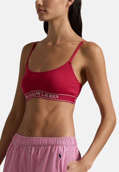 Röd sport-bh med tunna band och en logotyptryckt resår. Tyget är mjukt och elastiskt. Matchas med randiga pyjamasshorts.