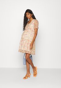 Vestido floral em rosa claro com mangas curtas bufantes e uma barra assimétrica. Combinado com sandálias de tiras laranja e uma mala azul clara.