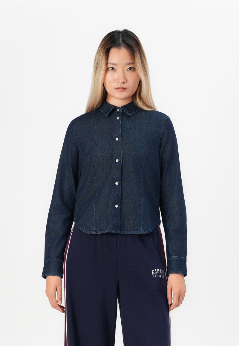 Dark denim button-up shirt with a collared neckline, long sleeves, and a cropped hem, featuring silver snap buttons along the front.