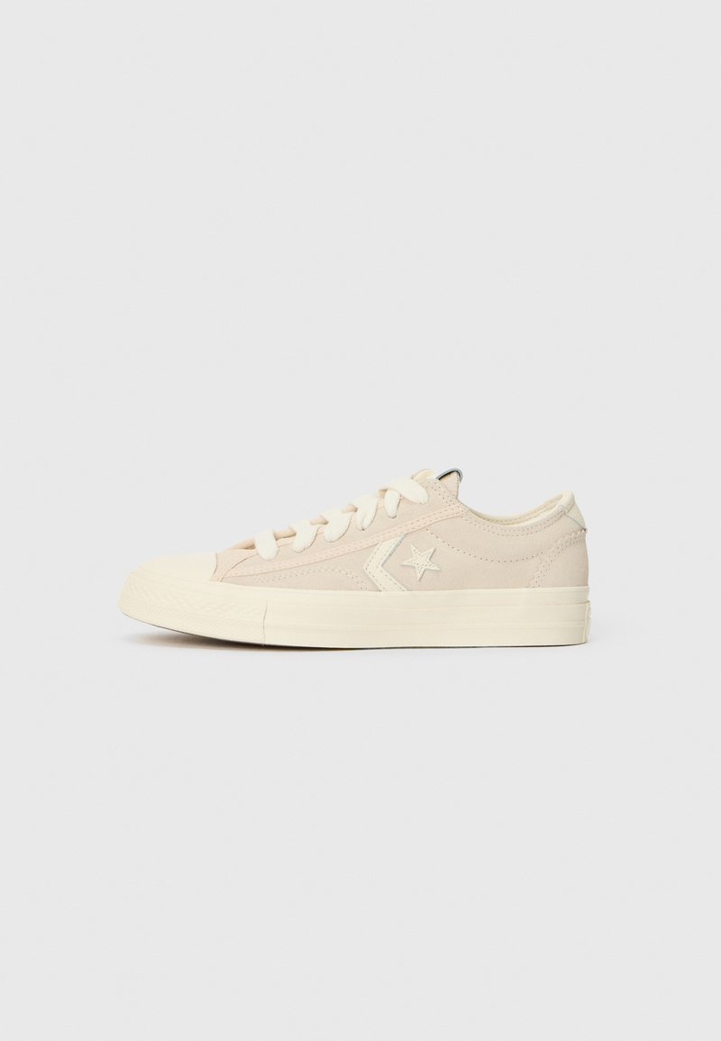 Baskets basses en toile beige avec lacets blancs, logo étoile et chevron sur le côté, et semelle épaisse en caoutchouc blanc sur fond gris clair.