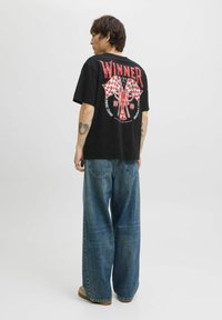 Sort bomulds-T-shirt med et rødt grafisk print af et trofæ og ternede flag på ryggen. Parret med brede jeans i blå.