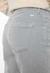 Jeans in denim grigio con design aderente, due tasche posteriori e cuciture sottili. Il materiale è morbido con una texture liscia.