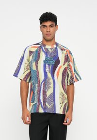 Kortærmet, multicolor t-shirt med abstrakte mønstre i lilla, grøn og fløde, med en blå grafisk tekstdetalje på forsiden.