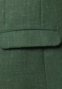 Zielona fakturowana tkanina w wzór w jodełkę, z detalem podwiniętego mankietu. Materiał wydaje się tkany i lekko szorstki.