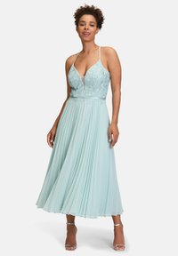 Robe plissée bleu clair avec corps en dentelle, décolleté en V profond et fines bretelles. Jupe fluide atteignant mi-mollet, avec des détails en dentelle délicate.