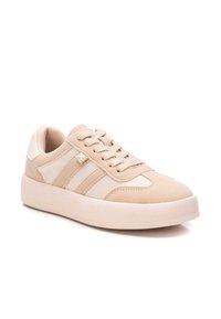 Zapatillas beige con parte superior de ante y cuero liso, con tres rayas texturizadas, puntera redondeada y una gruesa suela de goma blanca.
