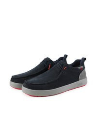 Scarpe in suede blu navy con suole in gomma grigia e dettagli rossi. Presentano un design slip-on con una cucitura e un dettaglio di allacciatura frontale.