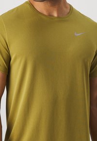 Camiseta de manga corta Nike de color verde olivo; tejido texturizado; escote redondo; presenta un pequeño logo gris en la parte superior del lado izquierdo del pecho.