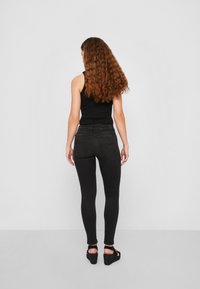 Jeans skinny negros con cintura de altura media y diseño clásico de cinco bolsillos, combinados con una camiseta de tirantes ajustada negra y sandalias de cuña negras.