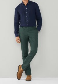 Camicia blu navy con bottoni, pantaloni verdi e scarpe in camoscio marrone. Vestibilità su misura, design classico, tessuto texturizzato. Aspetto semplice e elegante.