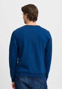 Plava majica s dugim rukavima i okruglim izrezom, izrađena od mekog materijala; ima glatku teksturu bez vidljivih logotipa.