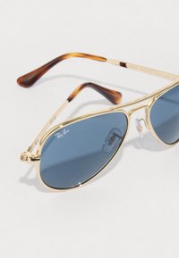 Occhiali da sole aviatore con montatura dorata, lenti blu e dettagli in tartaruga sulle astine. Presentano cuscinetti nasali trasparenti e il marchio Ray-Ban.