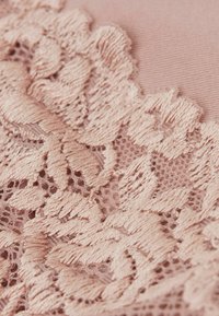 Delikat rosa spets tyg med intrikata blommönster och upphöjd broderi, som kontrasterar mot en slät bakgrund.