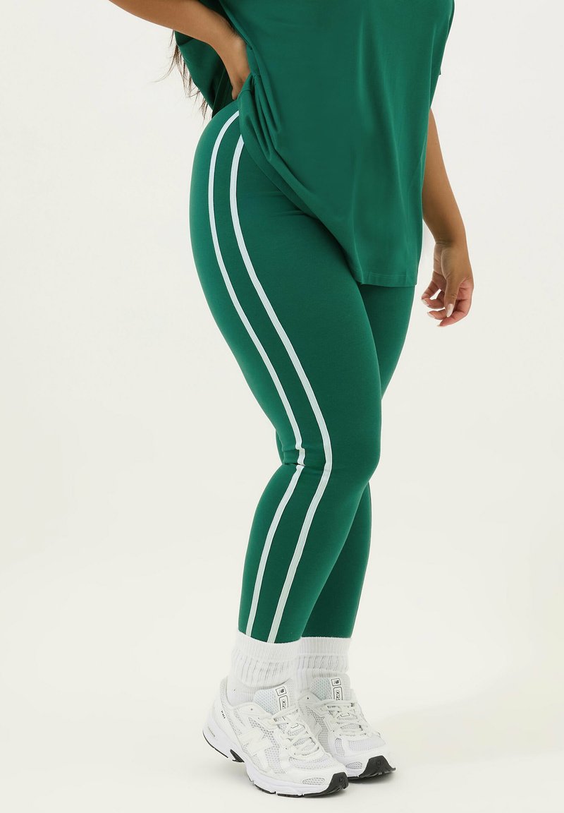 Gröna leggings med vita sidostäppar, stretchy material, hög midja, kombinerat med vita träningsskor och tjocka strumpor.