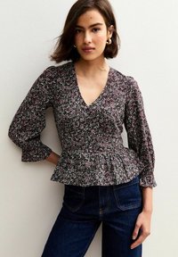 Zwarte bloemen peplum blouse met een diepe V-hals, puffed mouwen en ingewikkelde patronen in roze en groen. Gepaard met donkere jeans.