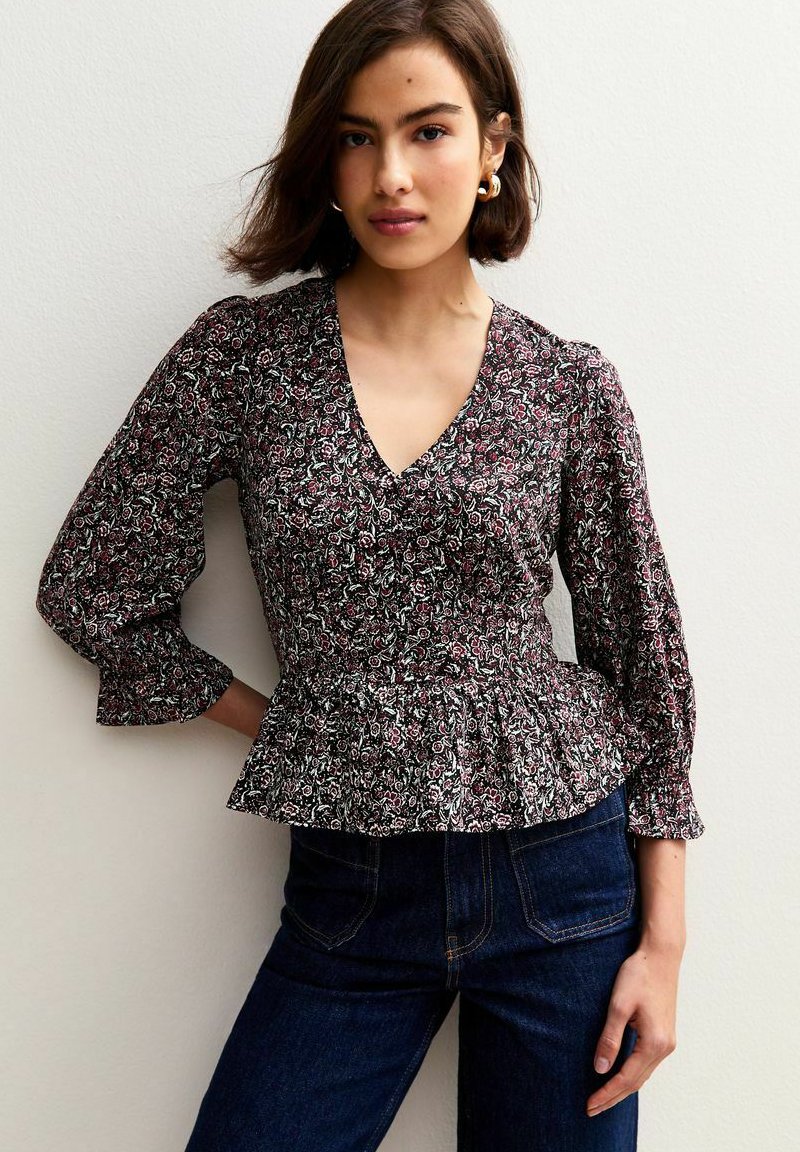 Zwarte bloemen peplum blouse met een diepe V-hals, puffed mouwen en ingewikkelde patronen in roze en groen. Gepaard met donkere jeans.