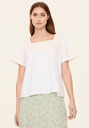 Top bianco a maniche corte con scollatura quadrata e dettagli ricamati arancione chiaro. Design morbido e ampio, texture soffice, abbinato a una gonna con fantasia floreale.