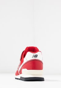 Sneaker New Balance rouge et blanc vu de l'arrière sur une surface blanche avec une semelle noire et une doublure en mesh visible à l'intérieur.