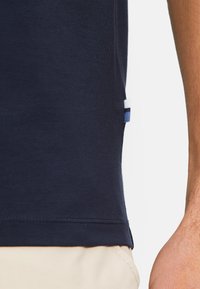 Himmelblaues Baumwoll-T-Shirt mit einer Seitennahtdetails und einem kleinen dreifarbigen Etikett am Saum. Weiche Textur und klassisches Rundhalsdesign.