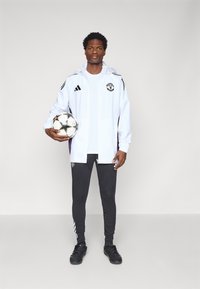 Adidas white jacket with black stripes and logo, matching black pants, holding a soccer ball with a star pattern.