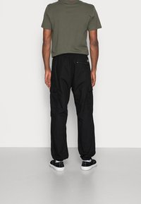 Zwarte cargobroek met elastische tailleband, twee zijzakken en één ritszak. Gepaarde met een olijfgroen T-shirt met korte mouwen.