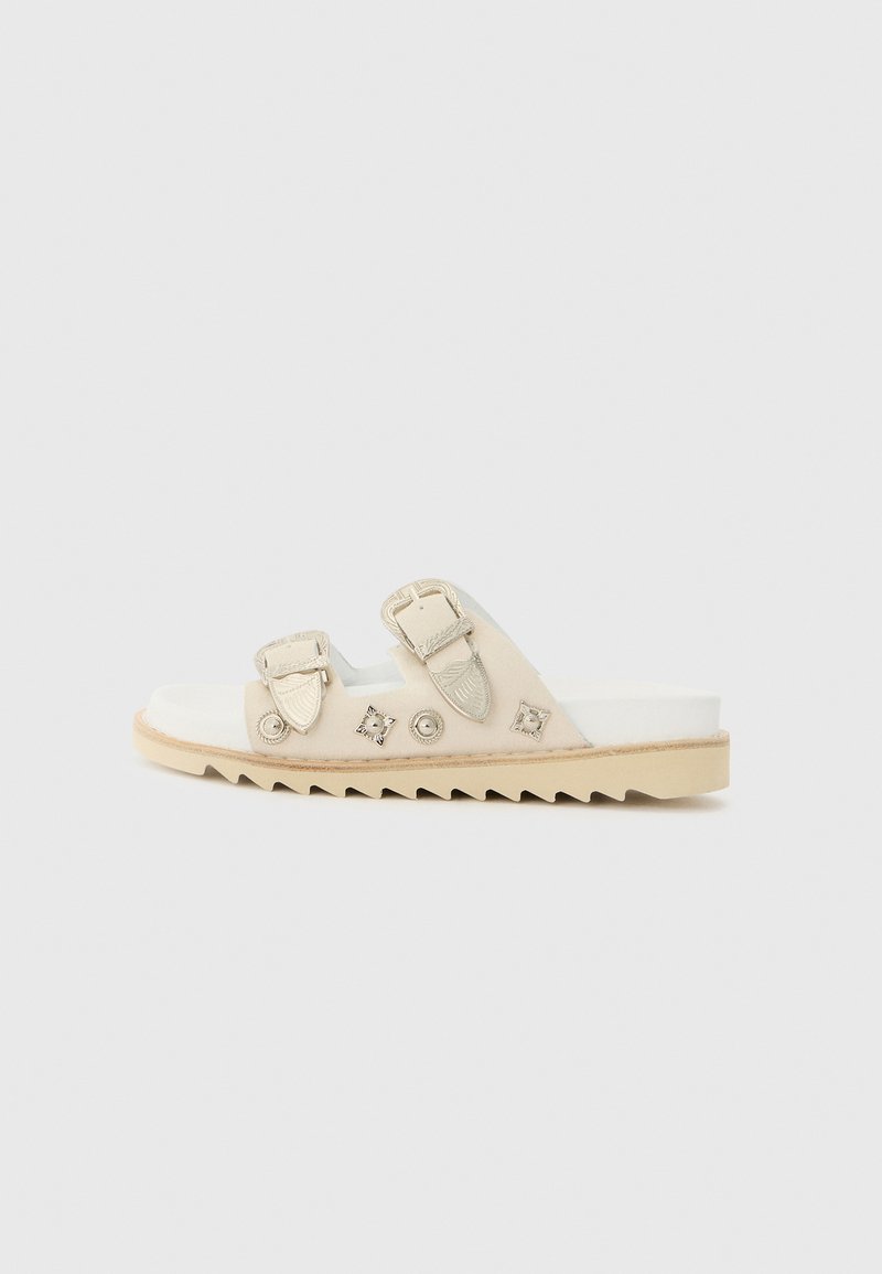 Beige slide sandal featuring two adjustable straps, decorative metal accents, a textured sole, and a soft footbed.