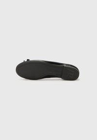 Black flat shoe with a smooth leather upper and a thin rubber sole. Features a small bow accent near the toe. Textured sole for grip.
