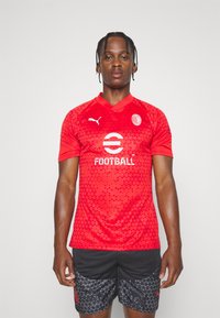 Maglietta da calcio rossa a maniche corte con un motivo testurizzato a triangoli, dotata di colletto tondo, logo Puma e testo bianco "FOOTBALL".