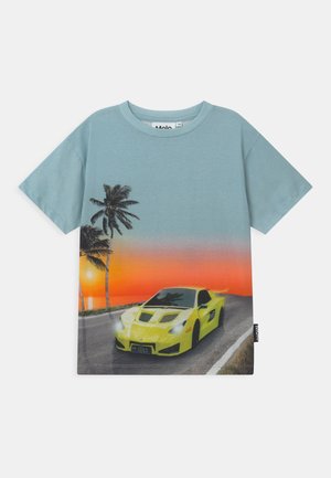 Camiseta azul de manga corta con un diseño de un coche deportivo amarillo en una carretera al atardecer con palmeras al fondo.