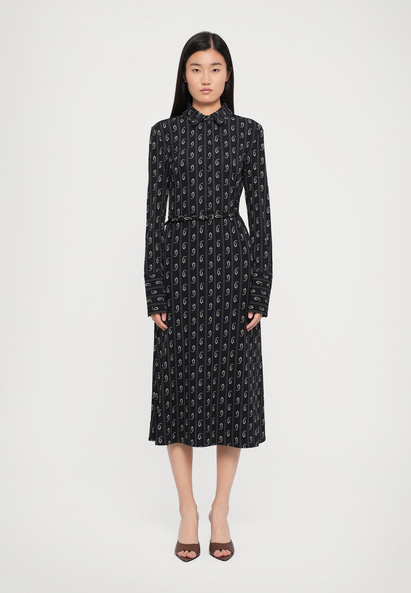 Abito a maniche lunghe con colletto in blu navy con motivi a spirale bianchi. Vita aderente con una cintura, gonna fluida e polsini con bottoni. Tessuto morbido e liscio.