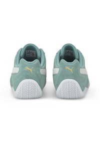 Baskets en daim vert avec des accents blancs, dotées d'une semelle en caoutchouc texturée et d'un détail de logo doré sur le talon. Vue arrière des chaussures.