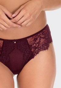 Burgundzka koronkowa bikini z przezroczystymi panelami, zdobiona kwiatowymi wzorami i małą kokardką na środku. Miękka tekstura materiału.