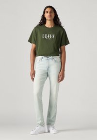 Grønn bomull T-skjorte med hvit tekst, kombinert med lyseblå denimjeans. Avsluttet med hvite sneakers og en avslappet passform.