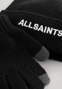 Černá pletená čepice s žebrovanou strukturou a bílým vyšitým nápisem "ALLSAINTS", doplněná černými rukavicemi s šedými špičkami.