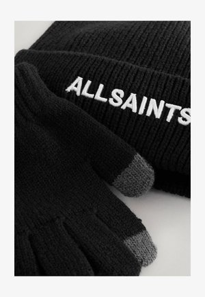 Fekete kötött sapka bordás textúrával és fehér "ALLSAINTS" hímzéssel, fekete kesztyűkkel, szürke ujjaikkal párosítva.
