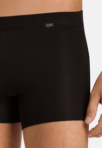 Black boxer briefs made of smooth fabric, featuring a logo tag, a snug fit, and ribbed texture along the waistband and hem.