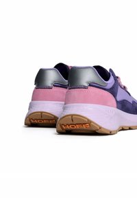 Violetit ja vaaleanpunaiset mokkakenkäparit, joissa on tyylikäs muotoilu, hopeiset yksityiskohdat ja teksturoitu valkoinen pohja, jonka takana on oranssi "HOFF" -logo.