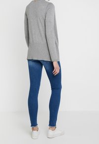 Grå långärmad topp med ribbad textur, kombinerad med blå skinny jeans med rå kant och vita sneakers.