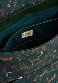 Zelena torba s motivima prirode, koja prikazuje lisice, jelene i ptice. Unutrašnjost je obložena tirkiznom tkaninom s suptilnim sjajem. Vidljiva oznaka.