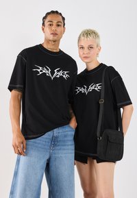 Sorte oversized t-skjorter med hvit grafikktrykk, kombinert med lyseblå vide jeans og en svart crossover-veske.