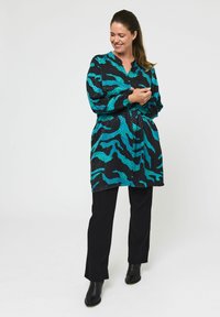 Sort tunika med turkise abstrakte mønstre og teksturerede detaljer, parret med sort lige ben-bukser og ankelsko.