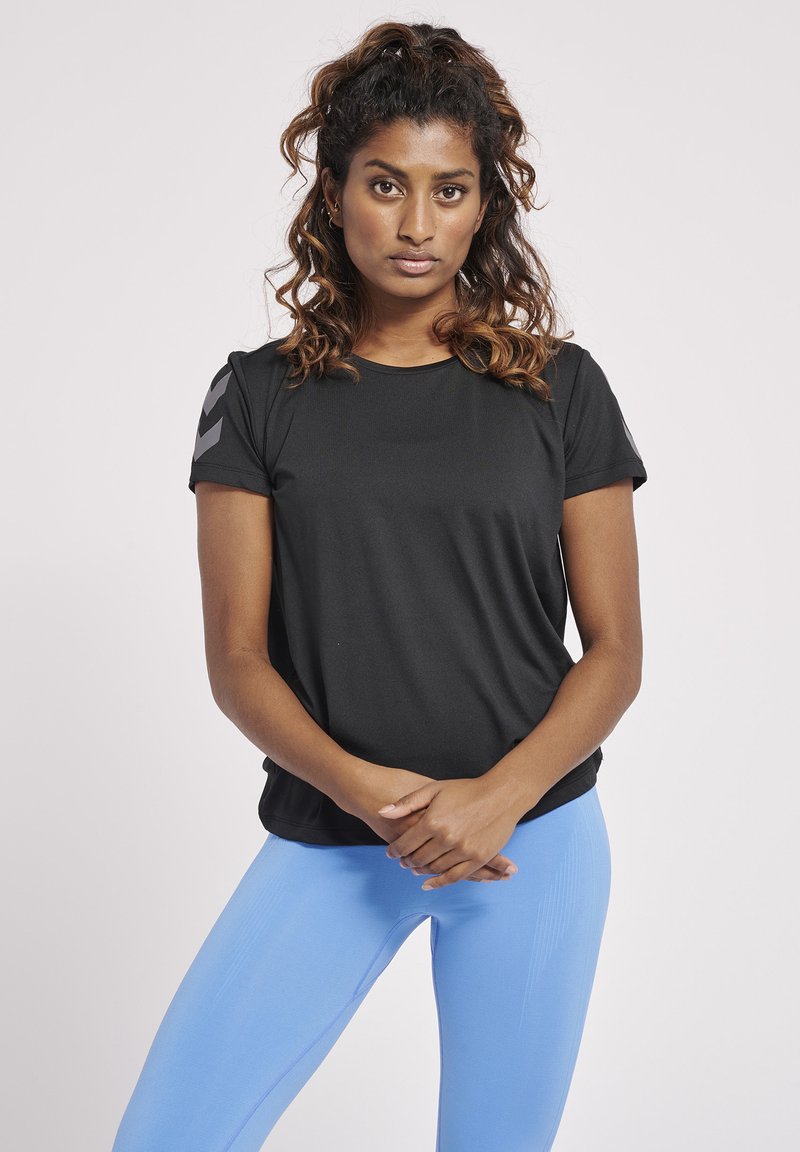 Schwarzes sportliches T-Shirt mit kurzen Ärmeln und kontrastierenden grauen Chevron-Akzenten an den Schultern, getragen mit hellblauen Leggings. Glatter Stoff und lockere Passform.