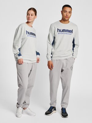 Mann und Frau stehen nebeneinander und tragen hellgraue Hummel-Sport-Sweatshirts und passende Jogginghosen mit Sneakers.