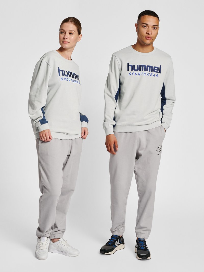 Mand og kvinde stående side om side iført lysegrå hummel sportssweatshirts og matchende joggingbukser med sneakers.