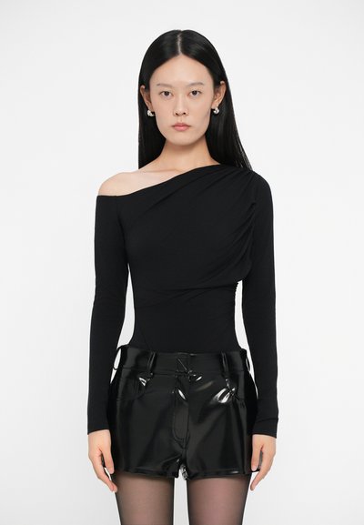 Bodysuit negro de manga larga con escote asimétrico y diseño drapeado, combinado con pantalones cortos brillantes de talle alto en negro. Textura suave.
