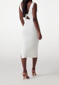 Vestido midi blanco con textura acanalada, con una alta abertura y detalle en la espalda descubierta. Combinado con tacones de aguja marrones, que destacan una silueta elegante.